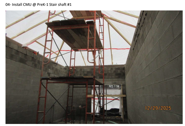 Scaffolding inside a stair shaft under a tent for CMU installation.